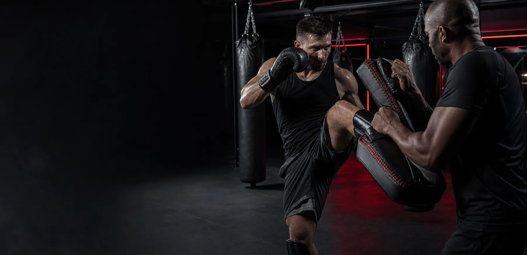 Atleta entrenando kick boxing con un coach en un gimnasio negro con luces rojas